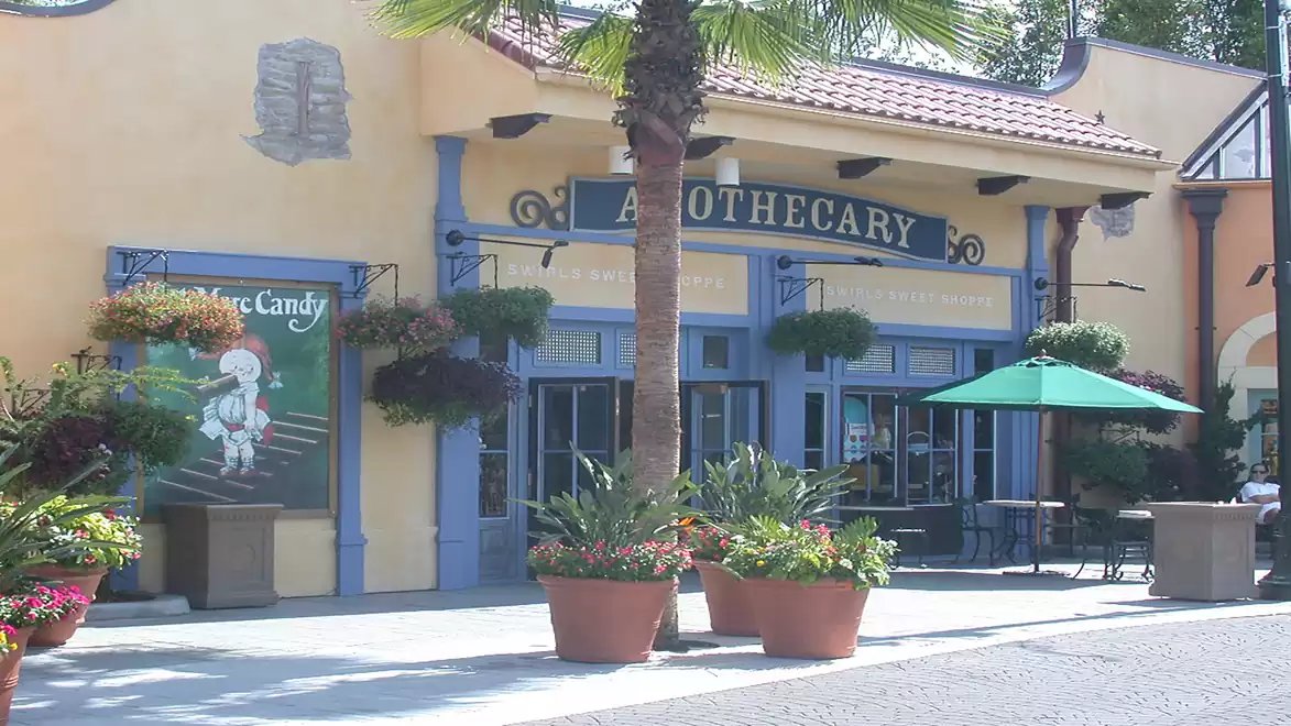 A small shop with 'Apothecary' written on the facade, surrounded by plants and a sun umbrella.