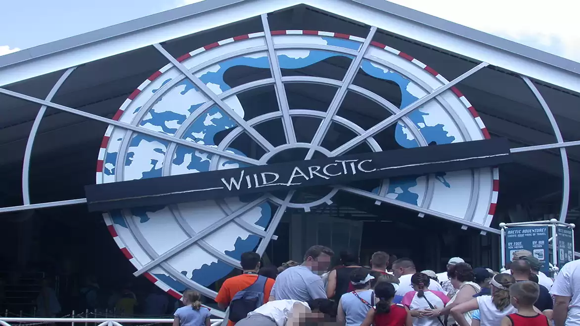 People standing in line at the entrance of Wild Arctic with a large wheel pattern in the background.