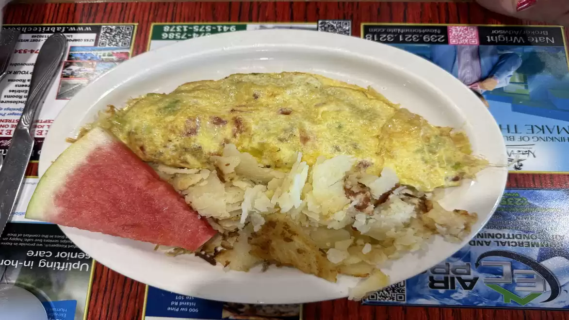 A breakfast plate with an omelette and a slice of watermelon on a restaurant table.