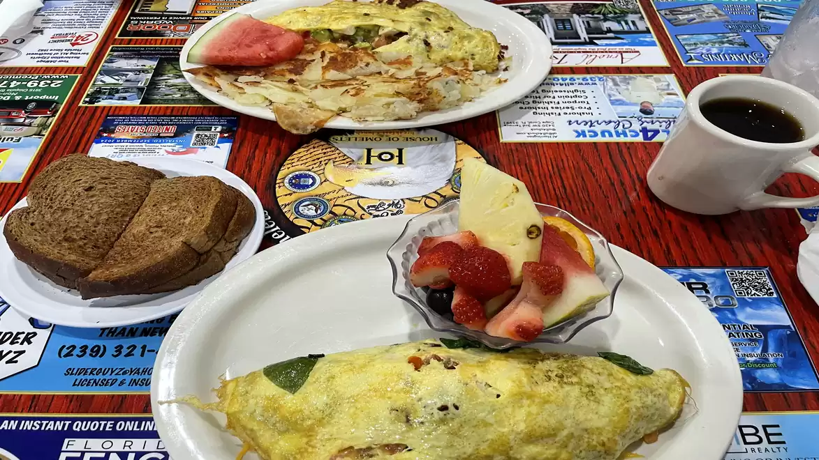 A breakfast table with an omelet, fruit bowl, toast, and a cup of coffee on a colorful tablecloth.