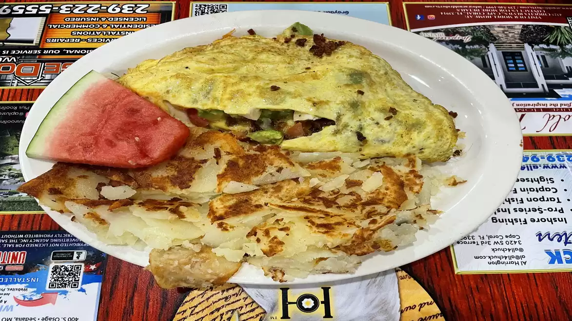 A plate with a stuffed omelet, served with hash browns and a slice of watermelon on a restaurant table.