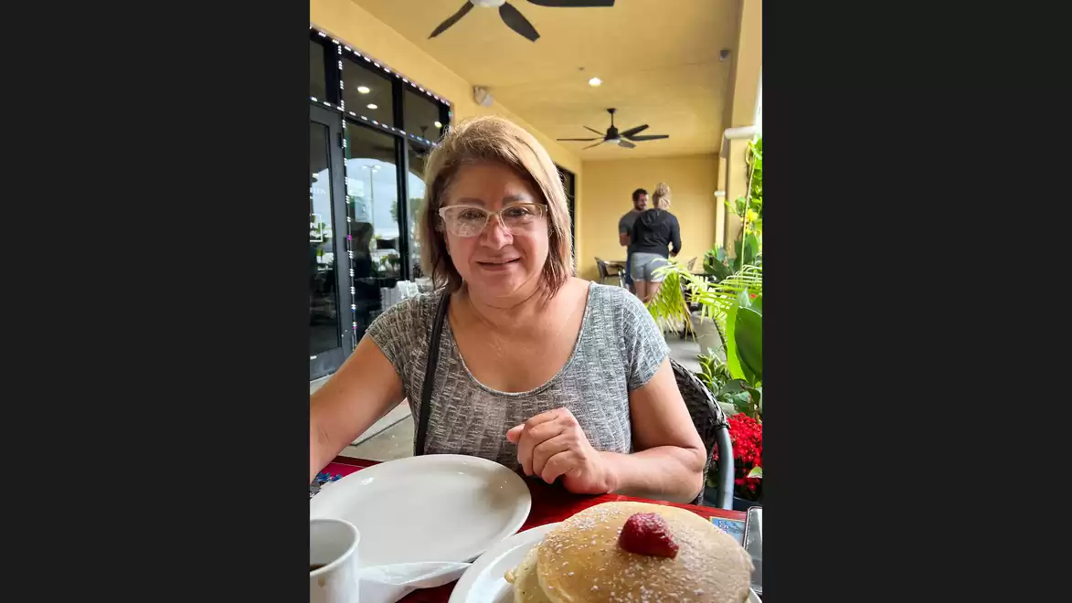 A woman sitting in a restaurant enjoying fried pastry with a strawberry on top.
