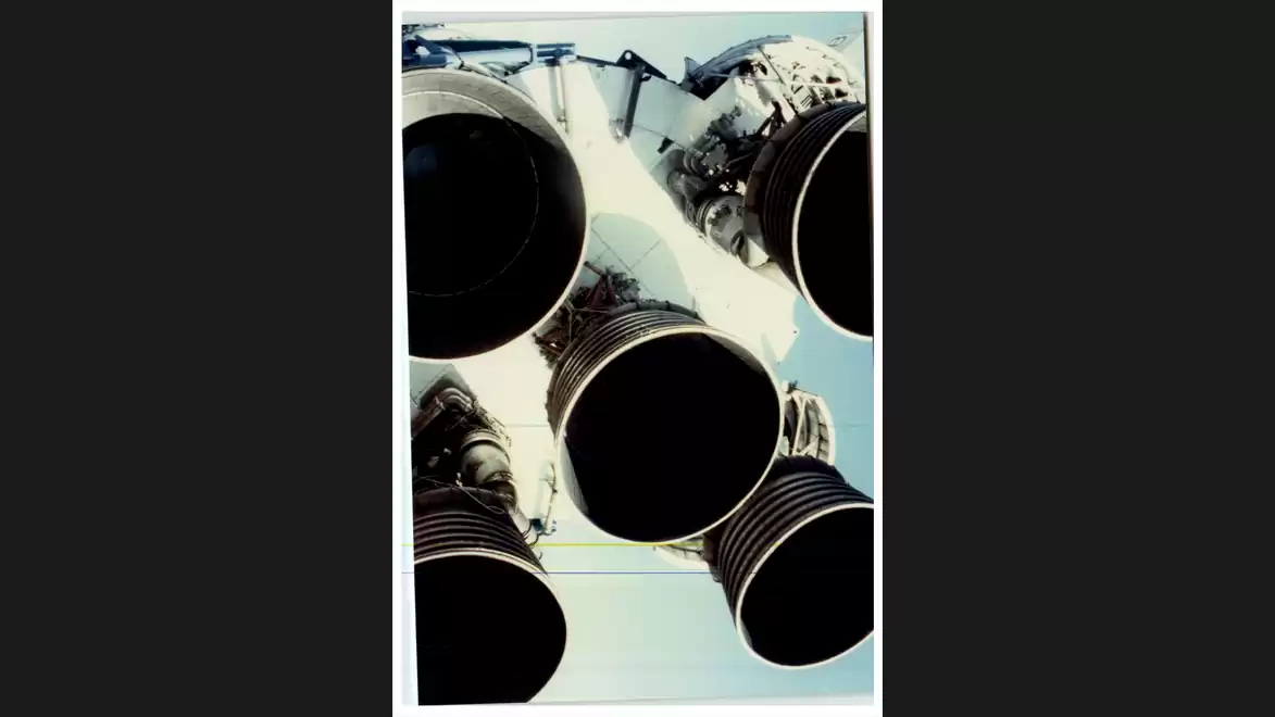 Close-up of five large rocket engines pointing downward against a blue sky.