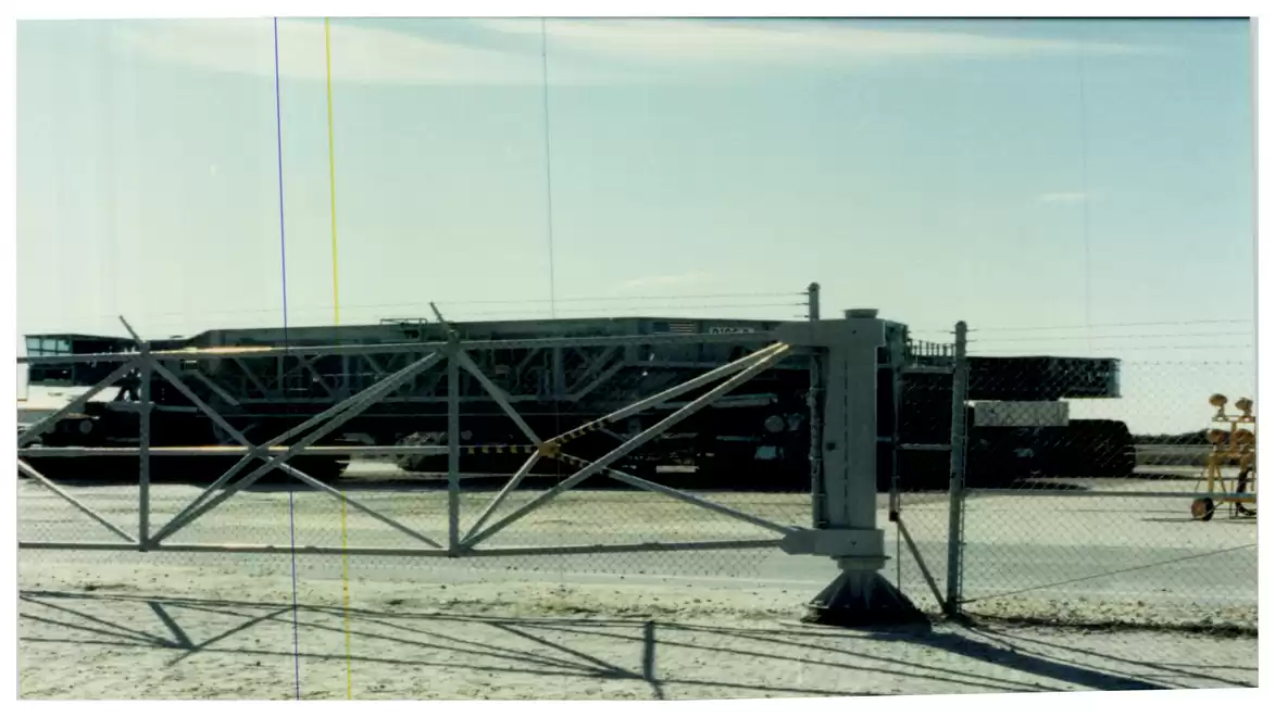 A large industrial vehicle behind a fence on an outdoor concrete area under a blue sky.