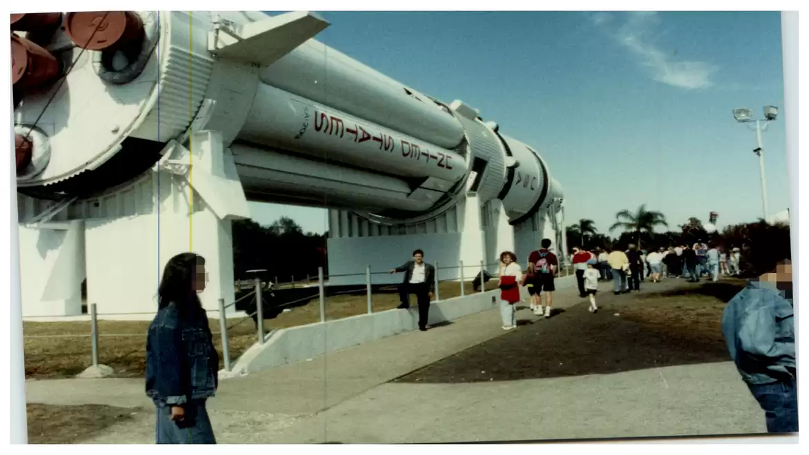A large rocket stands outdoors on an exhibition site, surrounded by visitors.