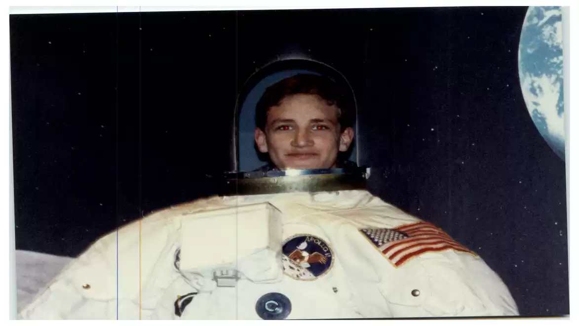A smiling man wearing an astronaut suit with an American flag and space emblems, standing in front of a starry sky with Earth in the background.
