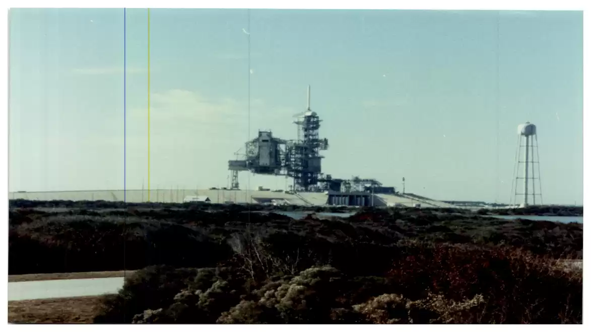 Rocket launch platform with water tower in the background, surrounded by natural vegetation under a clear sky.