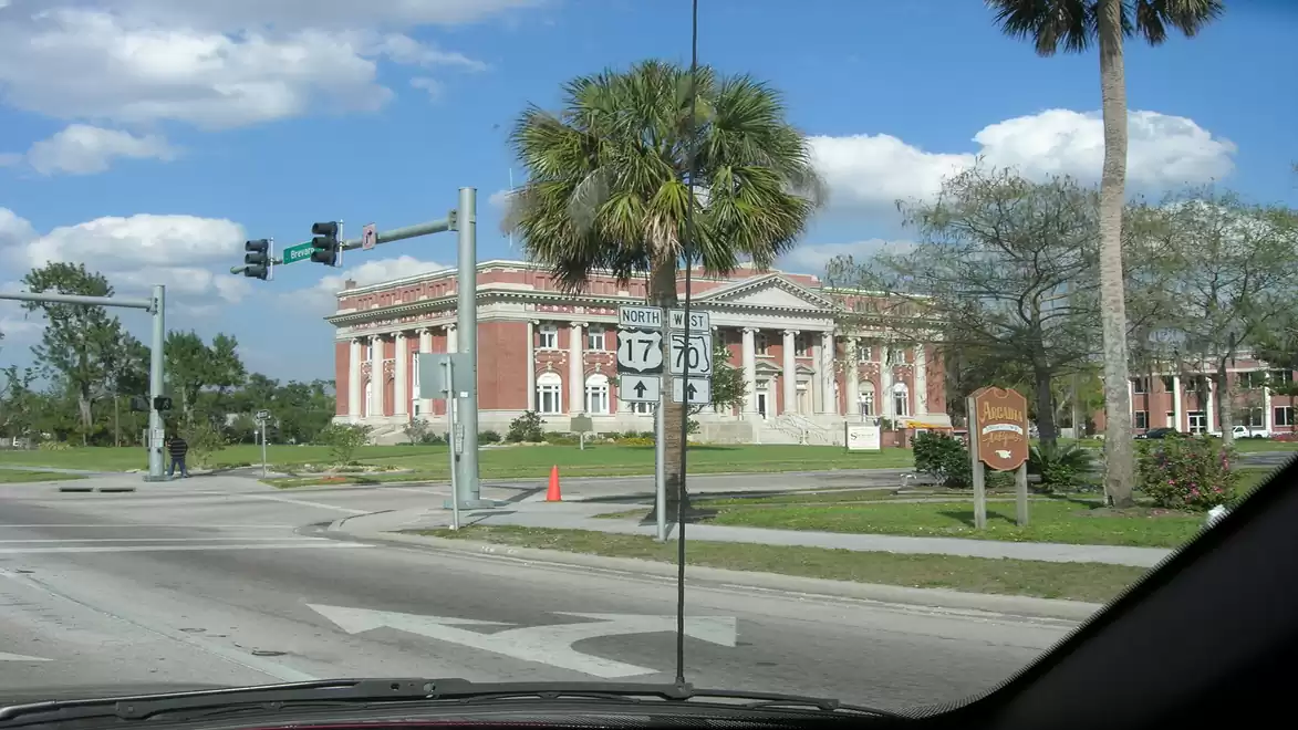 A historic building with impressive architecture is located at a street intersection with palm trees in the foreground and a clear blue sky in the background.