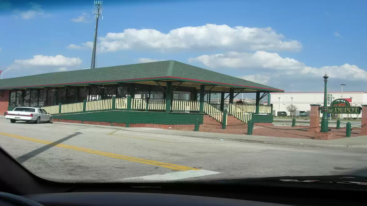A parking lot in front of a green building with yellow railings and a car on a sunny day.