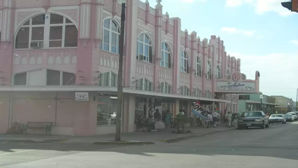 A pink building with classic Art Deco design on the street corner, surrounded by cars and people.