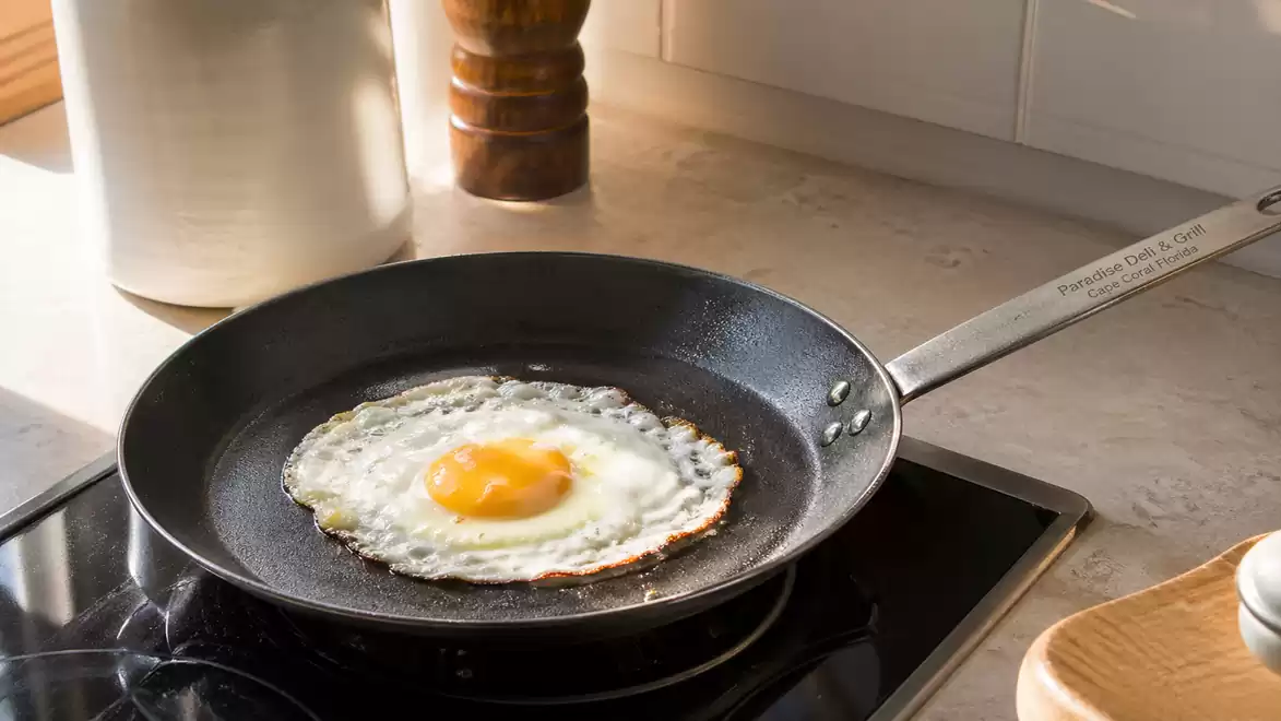 A fried egg cooks in a black pan on a stove, surrounded by kitchen utensils.