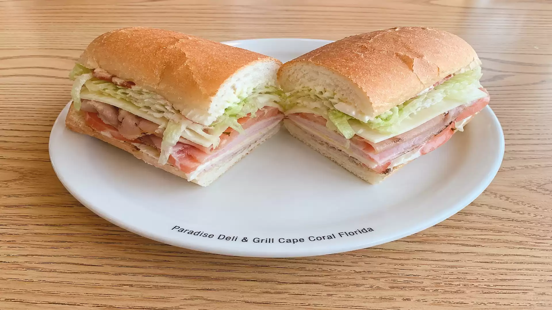 A halved sandwich with ham, cheese, and lettuce on a white plate, served on a wooden table.
