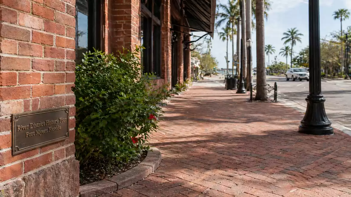 Brick building with a sidewalk and palm trees in a sunny urban setting.