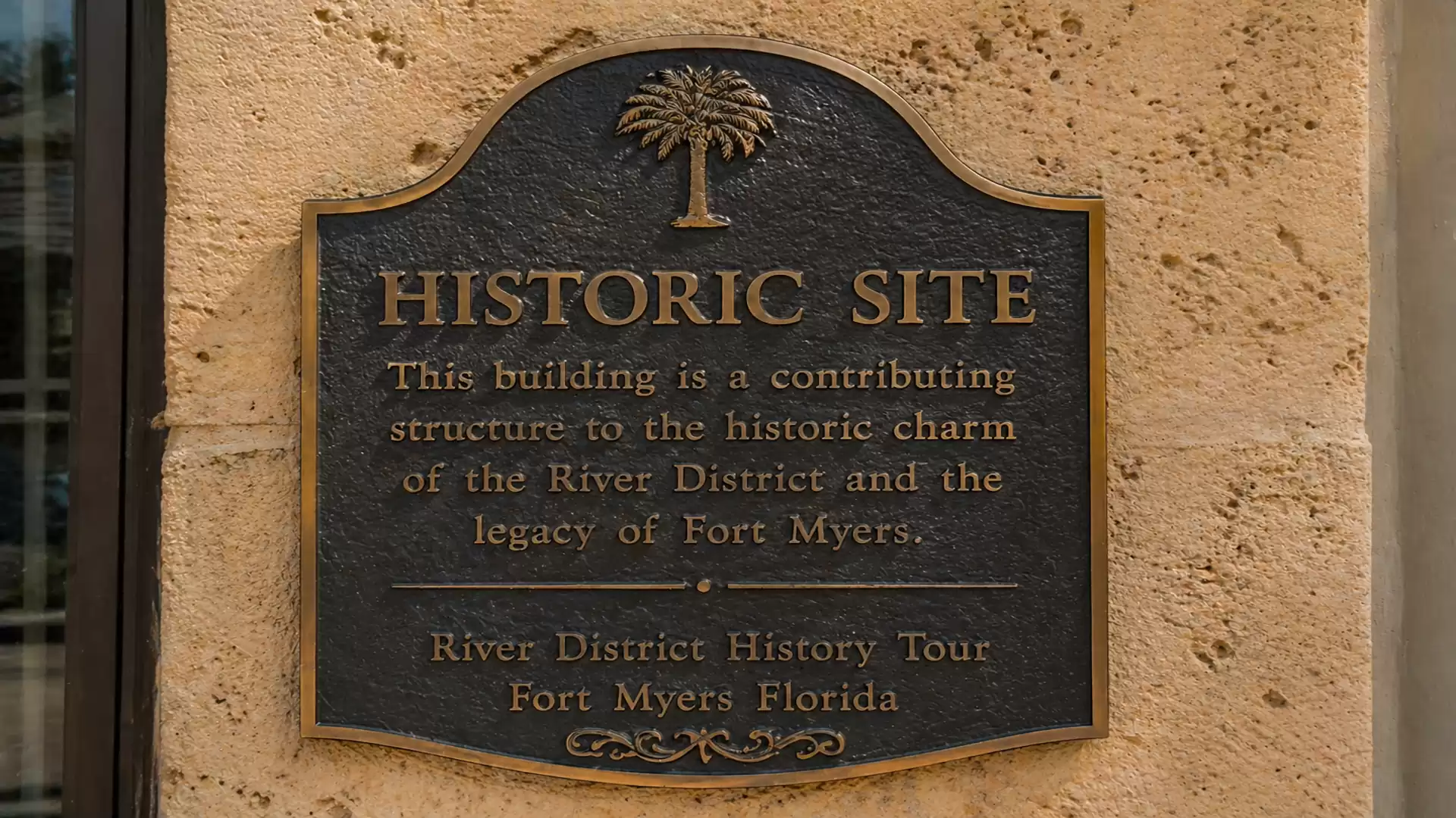 Bronze plaque on a wall with the inscription 'Historic Site' and a short text describing the building's significance to the historic charm of the River District in Fort Myers.