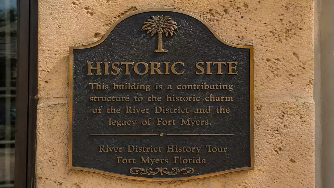 Bronze plaque on a wall with the inscription 'Historic Site' and a short text describing the building's significance to the historic charm of the River District in Fort Myers.