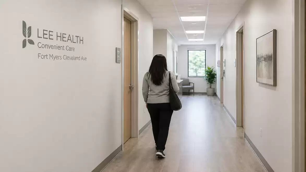 A person walks down a corridor of the Lee Health hospital. The walls are white and the floor is wooden. Plants and pictures are decoratively placed.