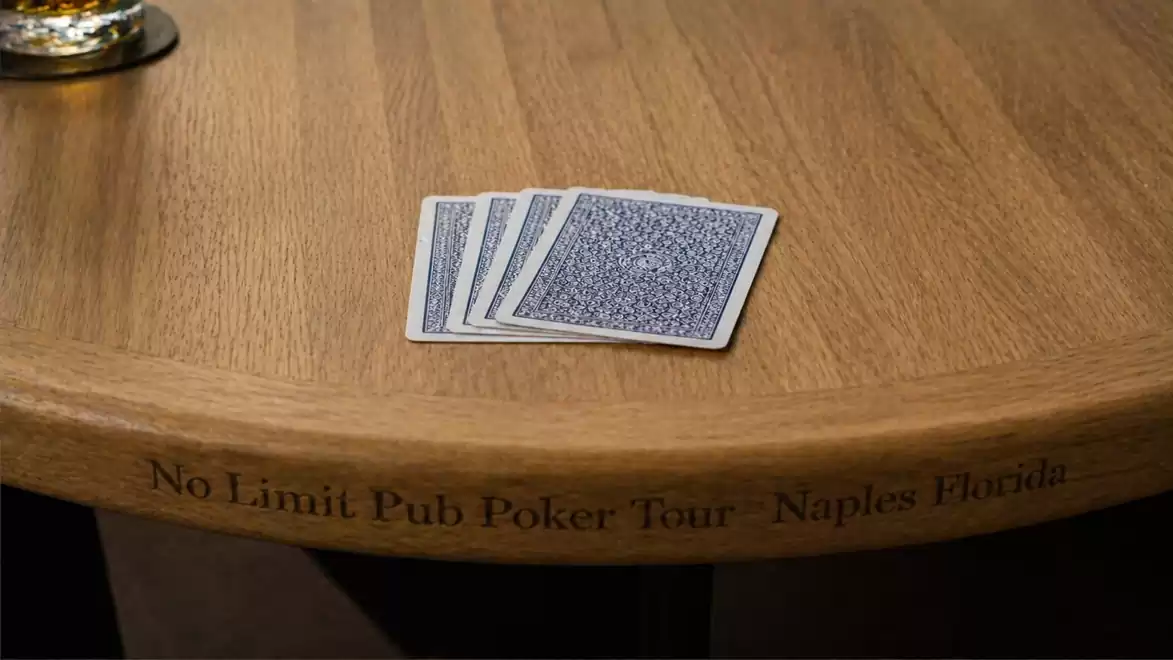 Close-up of a wooden table with a stack of playing cards, featuring the engraved text 'No Limit Pub Poker Tour Naples Florida' on the edge.