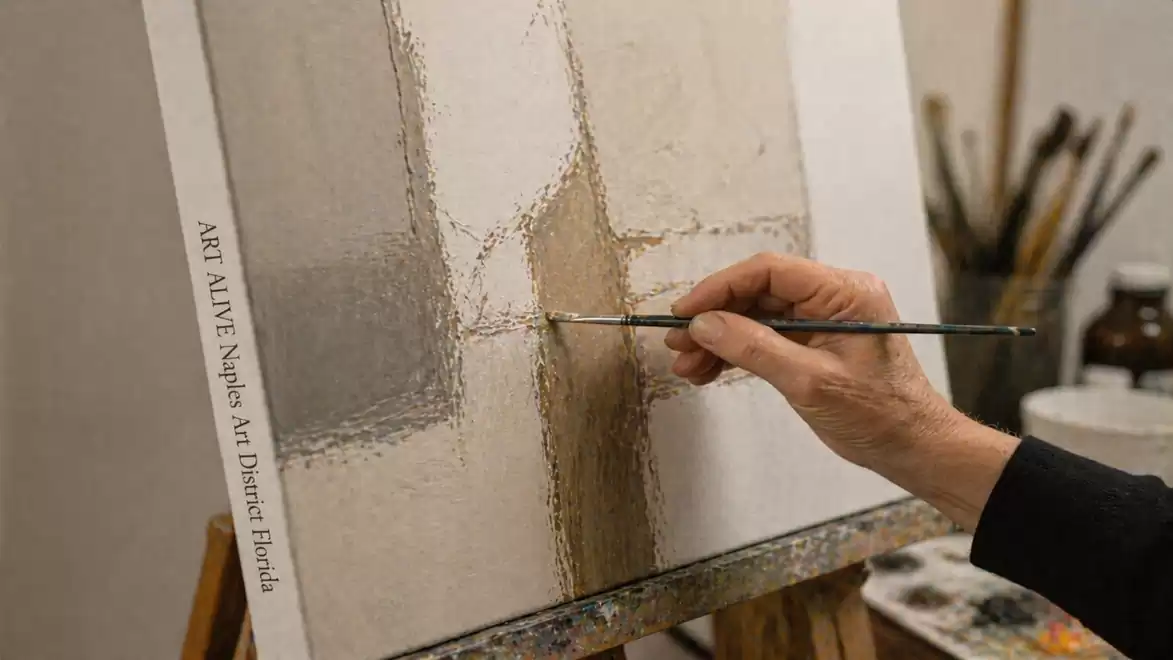 A close-up of a painter using a brush to create an abstract artwork on an easel.