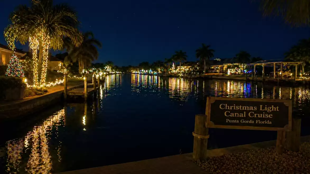 Night scene of a canal in Punta Gorda, Florida, adorned with glowing Christmas lights on palm trees and buildings.