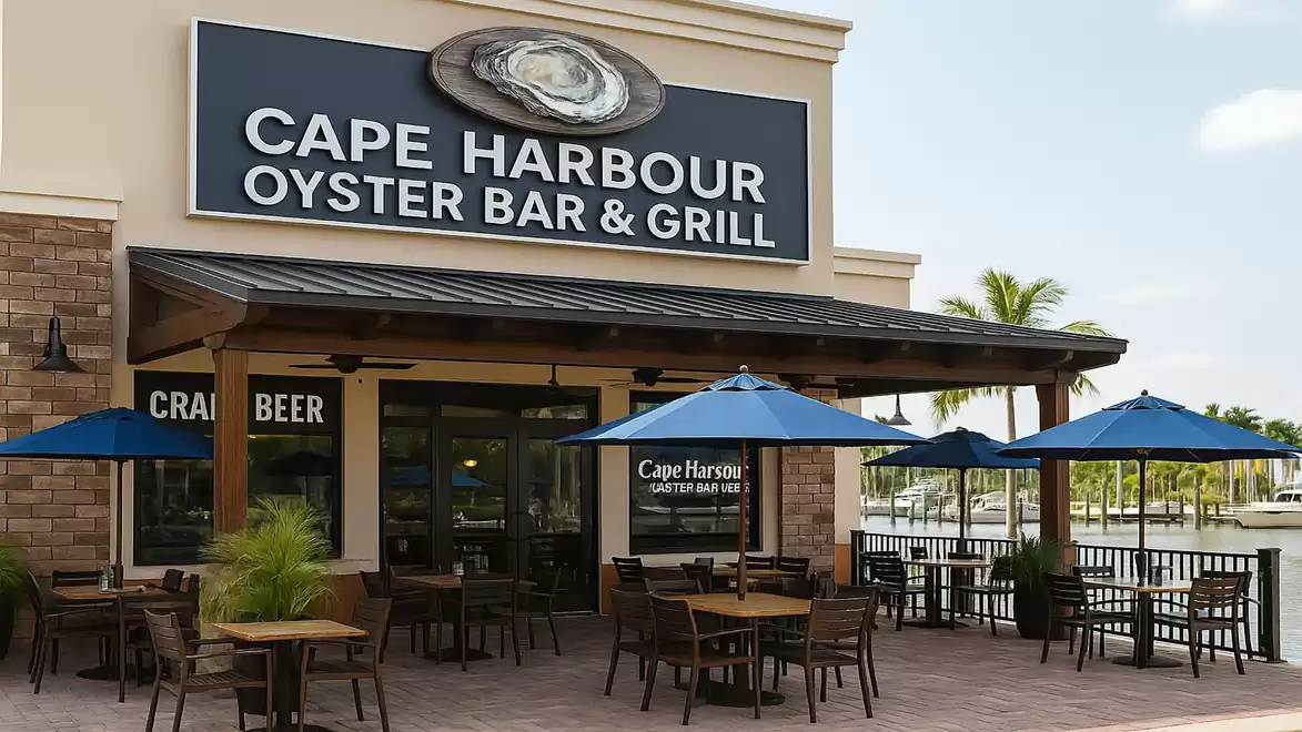 Exterior view of Cape Harbour Oyster Bar & Grill with blue umbrellas and outdoor seating in sunny weather.