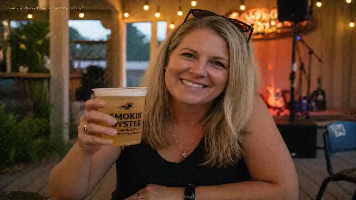 Blonde woman sitting in a cozy restaurant or café holding a drink. Lights and decorations are visible in the background.
