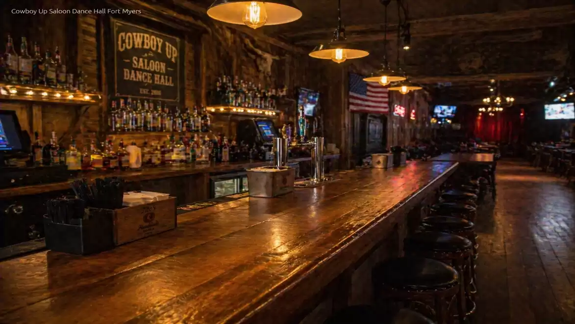 Interior view of a rustic saloon with a long wooden bar and stools, decorated with bottles and an American flag.
