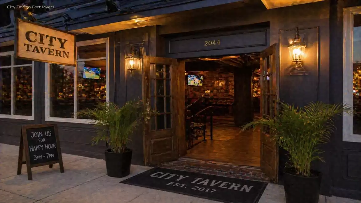 Entrance to the City Tavern bar at night, illuminated with warm lights, with plants on the sides and a welcome sign.