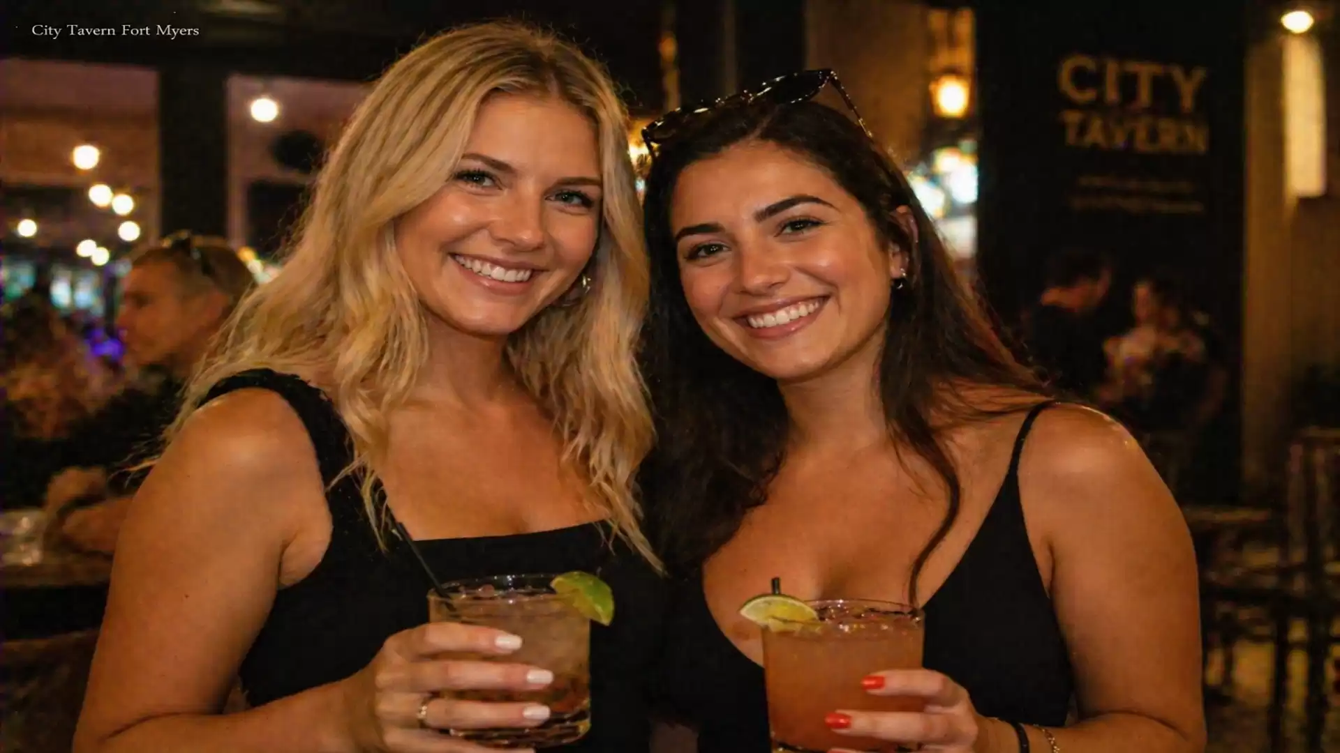 Two smiling women holding cocktails in a bar.