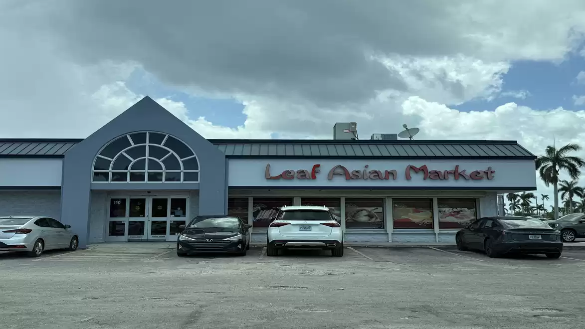 Exterior view of an Asian market with several parked cars in front under a cloudy sky.