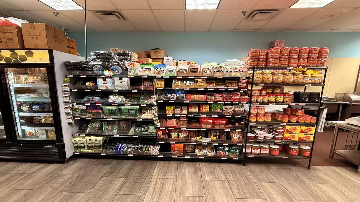Various packaged foods and canned goods on shelves in a small store with cool fluorescent lighting and wood flooring.