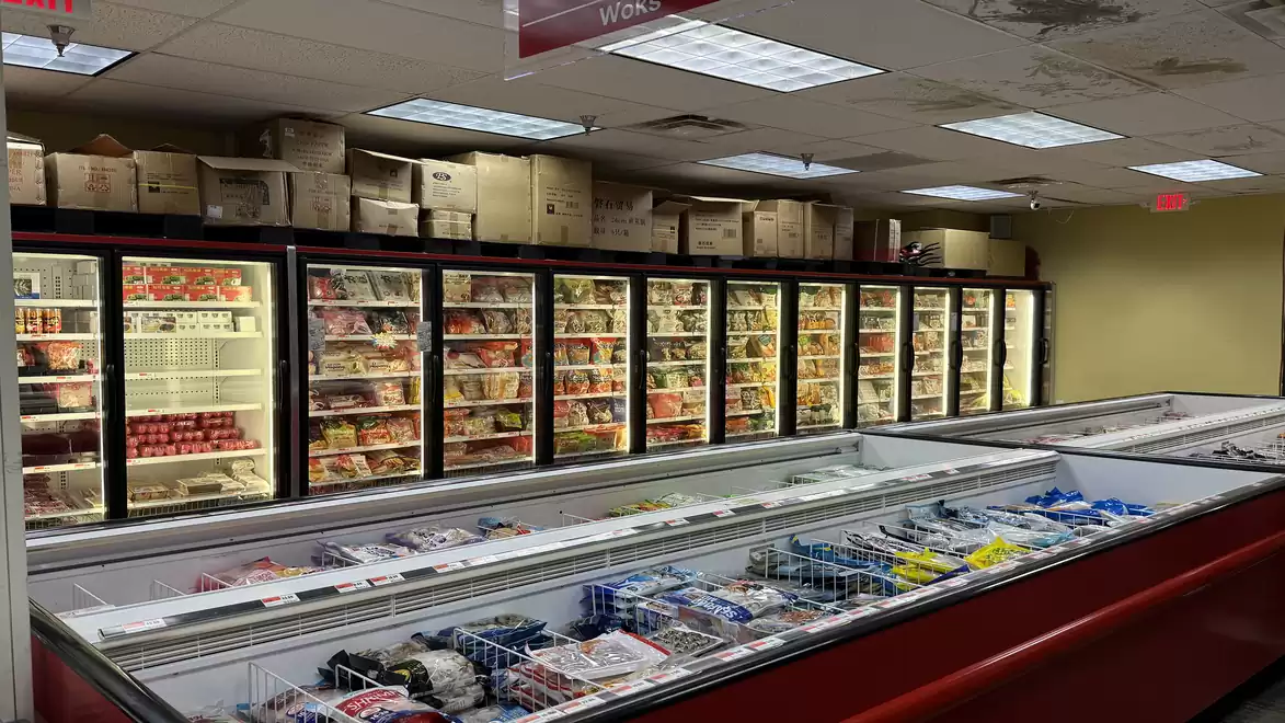 A supermarket with a long row of freezers filled with various food products and frozen pastries.