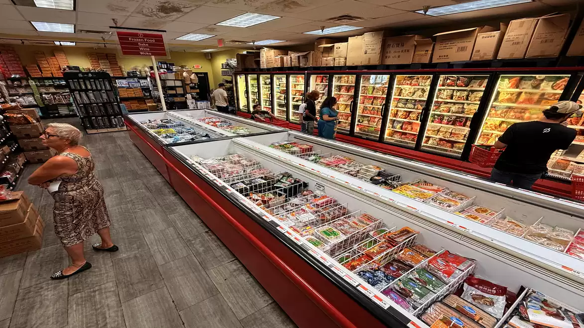 A supermarket with several freezers full of frozen products and shelves in the background. People are shopping.