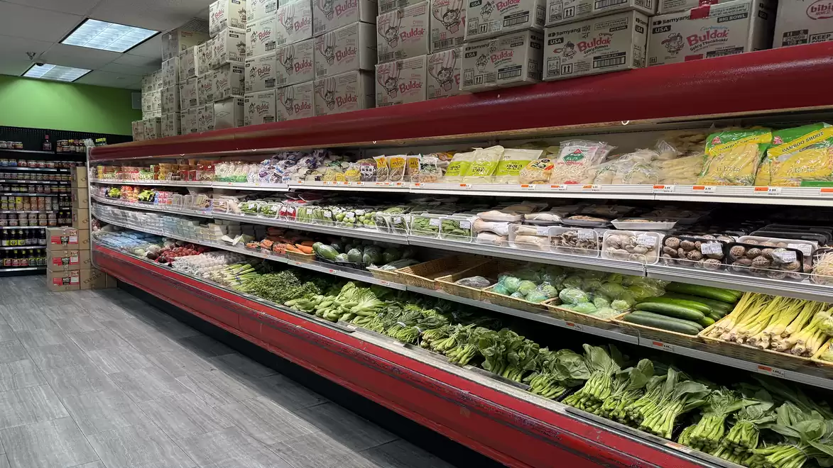 A supermarket aisle with shelves full of fresh vegetables and packaged foods.