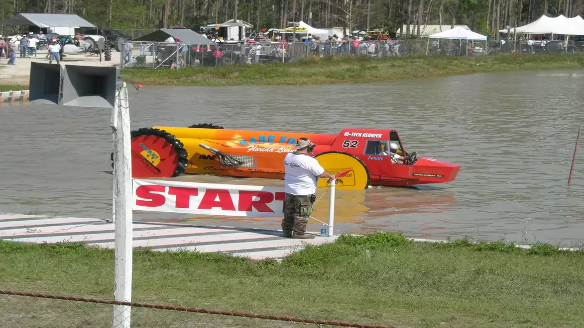 An amphibious vehicle prepares for a race taking place in the water. Spectators stand in the background.