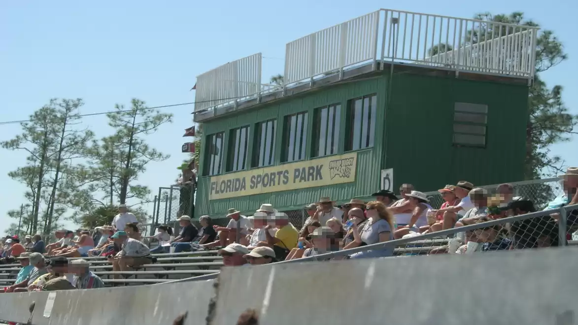 A crowd sits on bleachers in front of a building labeled 'Florida Sports Park' on a sunny day.