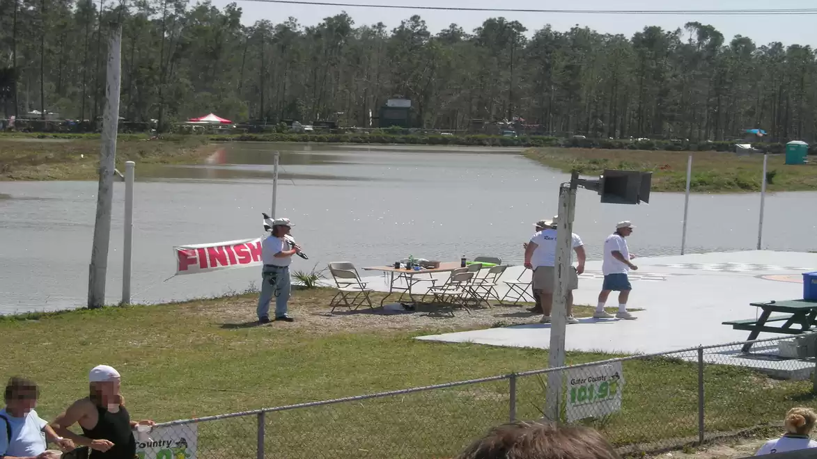 Image of a finish area at an outdoor event with a lake in the background and people gathering around a table.