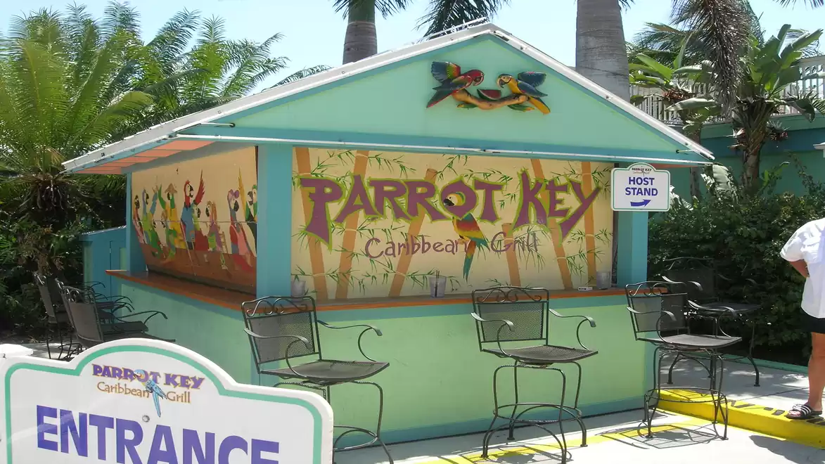 A tropical restaurant named Parrot Key Caribbean Grill with a colorful mural, palm trees, and pastel colors.
