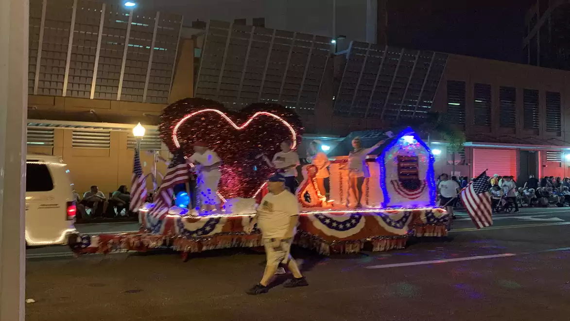 A decorated float with bright lights and American flags during a night parade.