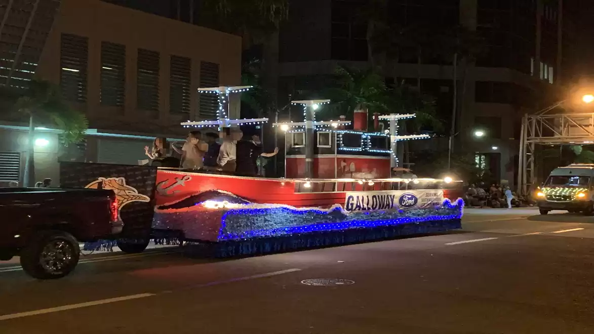 A decorated carnival float in the dark, adorned with lights and designed as a boat on a street.