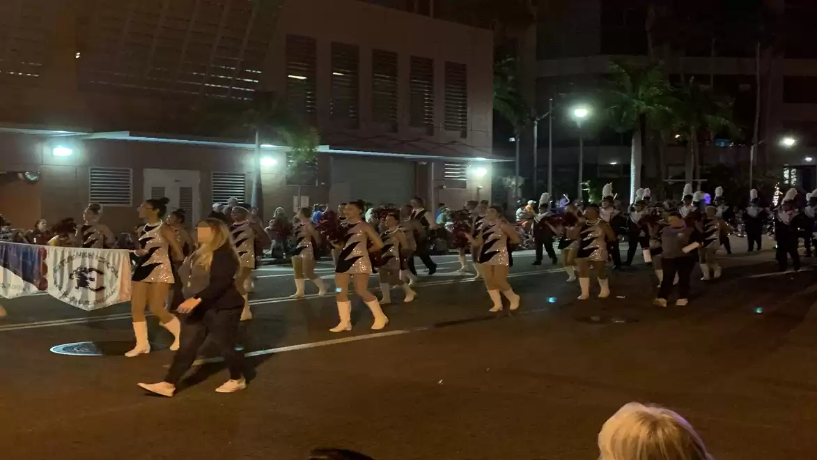 A group of people marching at a nighttime parade in a city on a lit street.