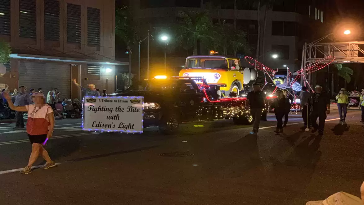 Night parade featuring an illuminated yellow vehicle on a float, accompanied by pedestrians.