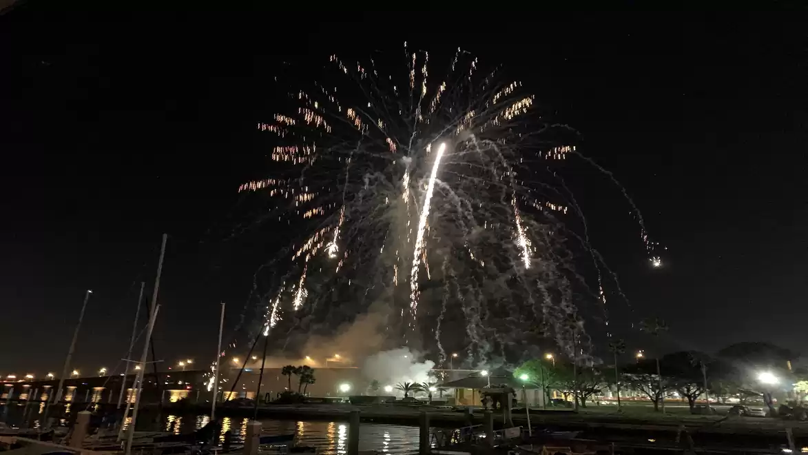 Nighttime fireworks over a marina with a dark sky and reflecting water.
