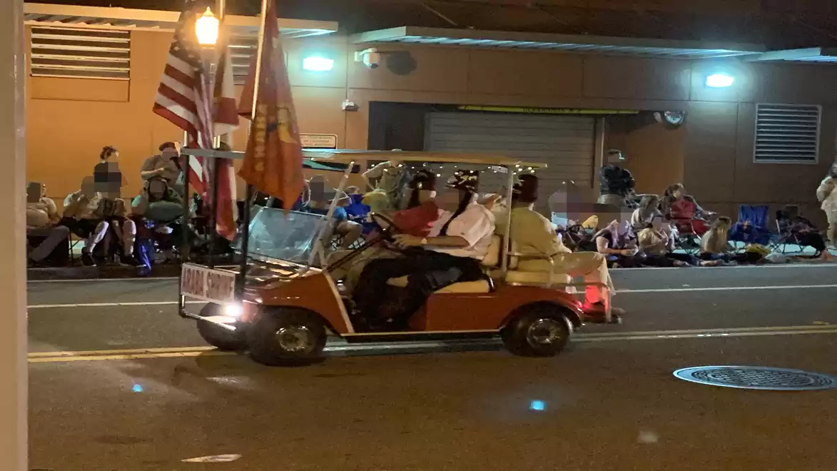 Small vehicle with flags driving past spectators at night.