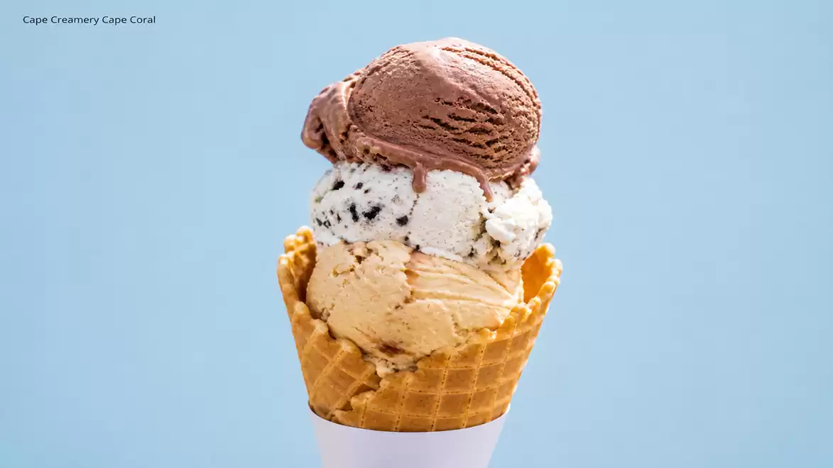 An ice cream cone with three scoops: chocolate ice cream, cookies and cream ice cream, and vanilla ice cream in a waffle cone against a blue background.