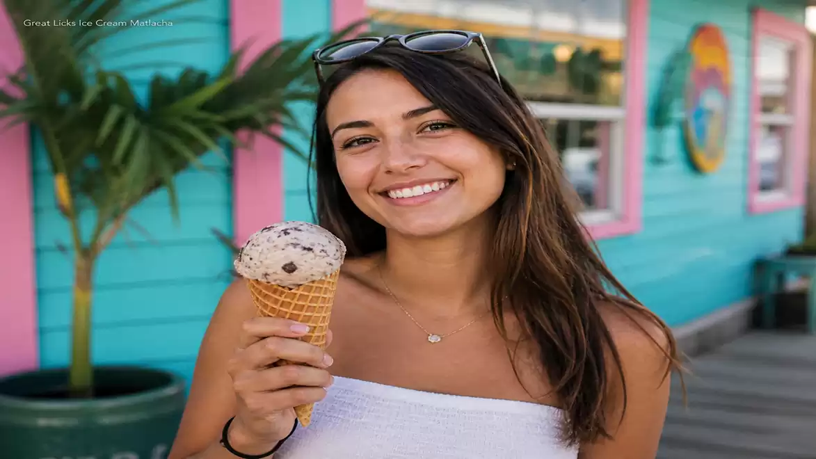 Woman with sunglasses in hair holding an ice cream in front of a colorful building.