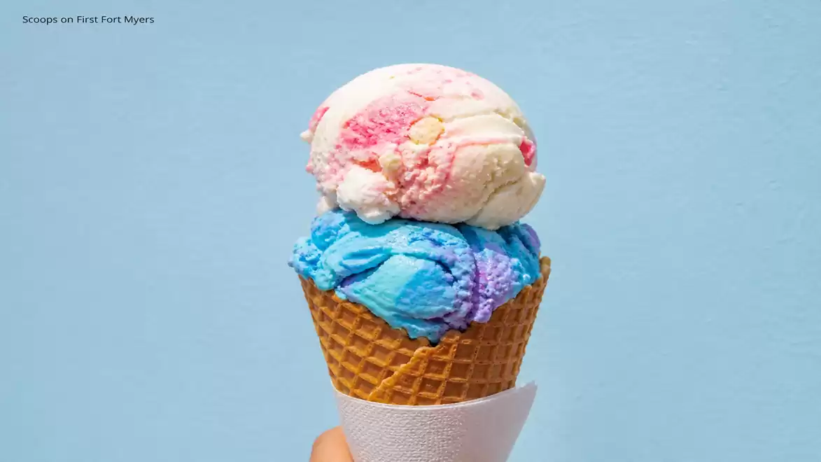 Close-up of an ice cream cone with two scoops, one blue and purple, and the other white and pink against a light blue background.