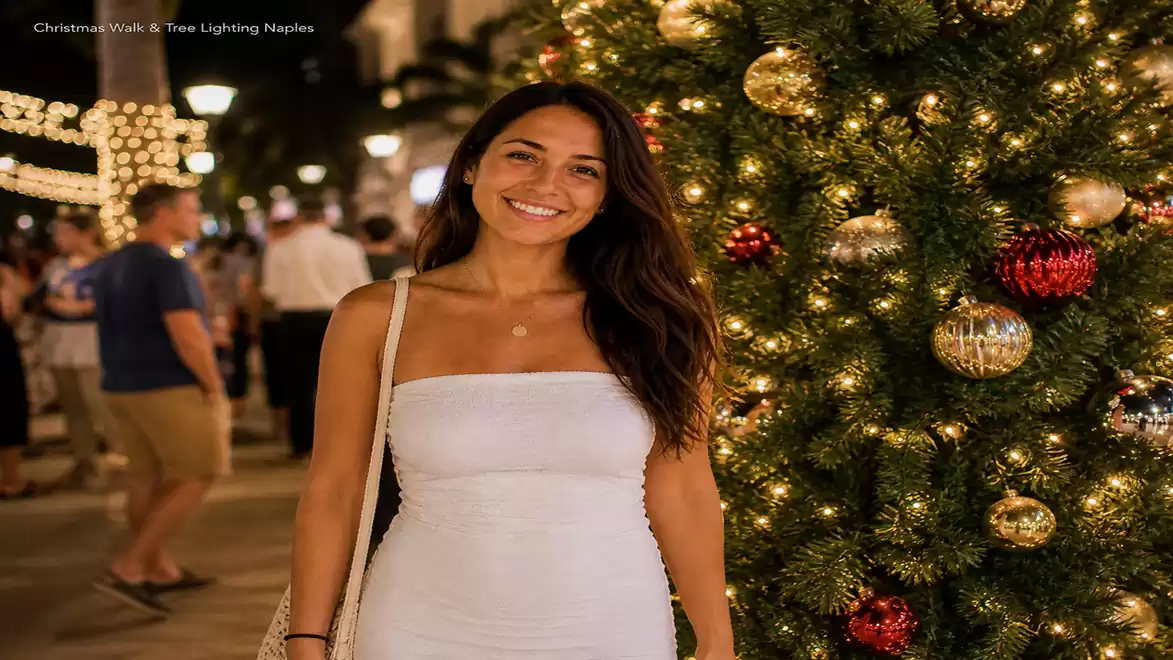 Woman in white dress smiling next to a decorated Christmas tree at night.