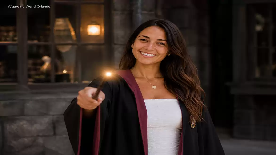 Young woman in Hogwarts robe holding a wand, smiling in a Harry Potter themed area.