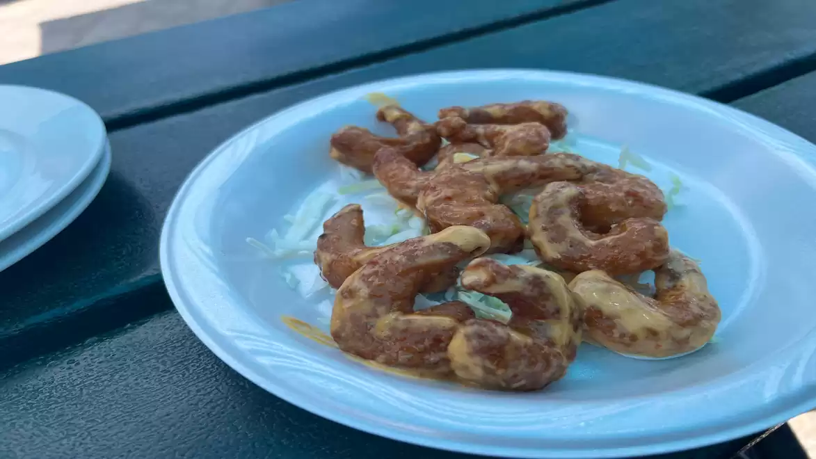 A close-up of fried shrimp on a white plate placed on an outdoor wooden table.