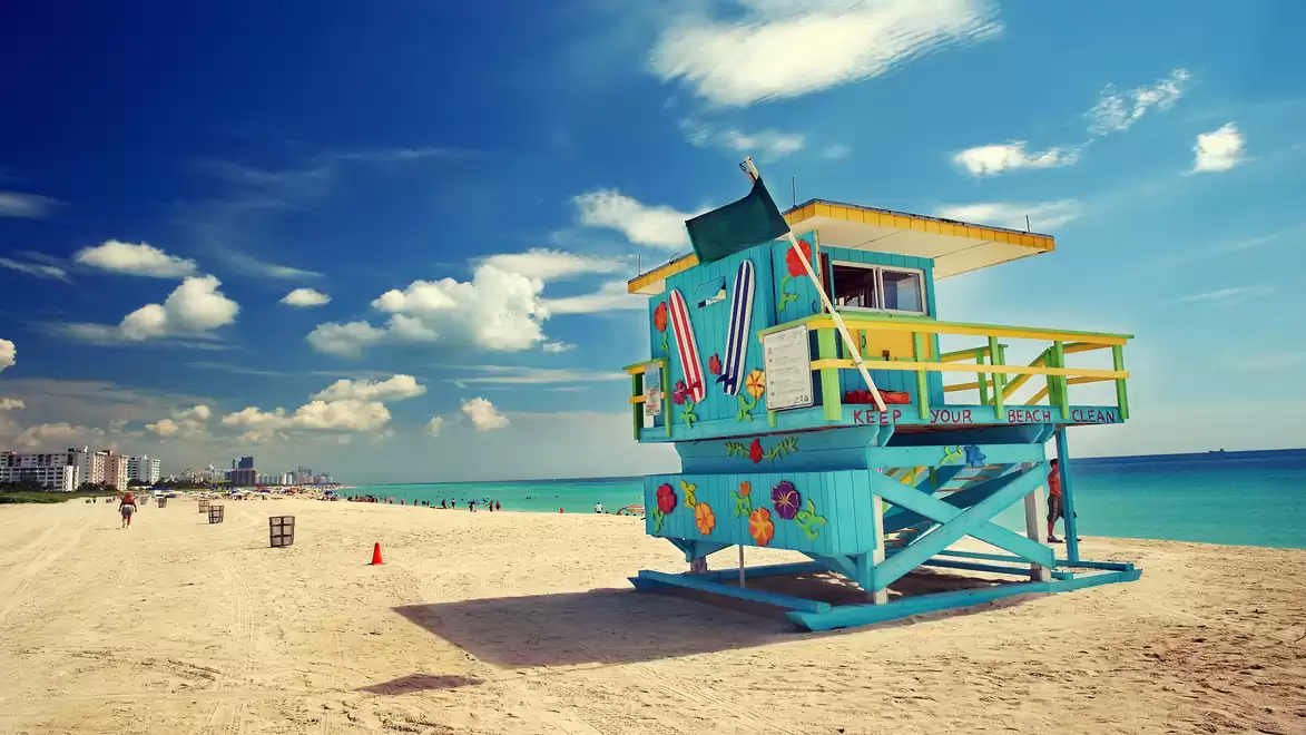 Colorful lifeguard hut on a sandy beach under sunny weather, with blue sky and clouds in the background.